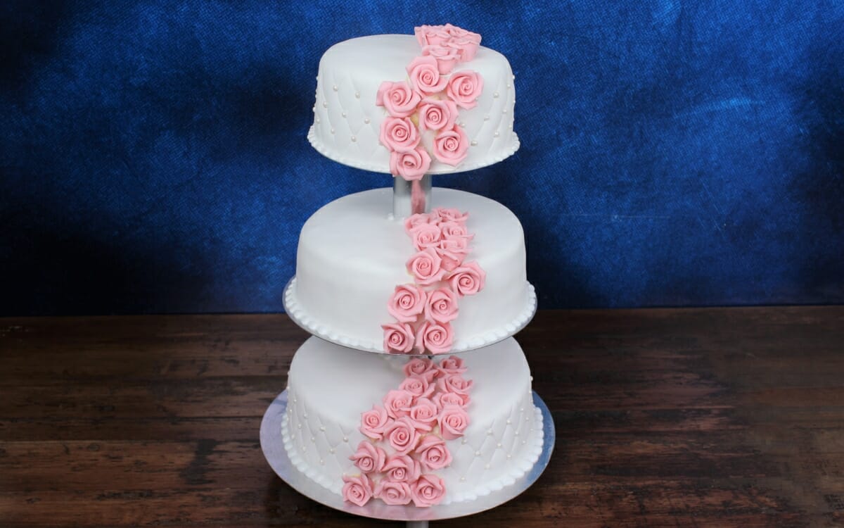 Bryllupskake i tre etasjer med rosa marsipanroser og hvitt marsipanlokk med putemønster og perler